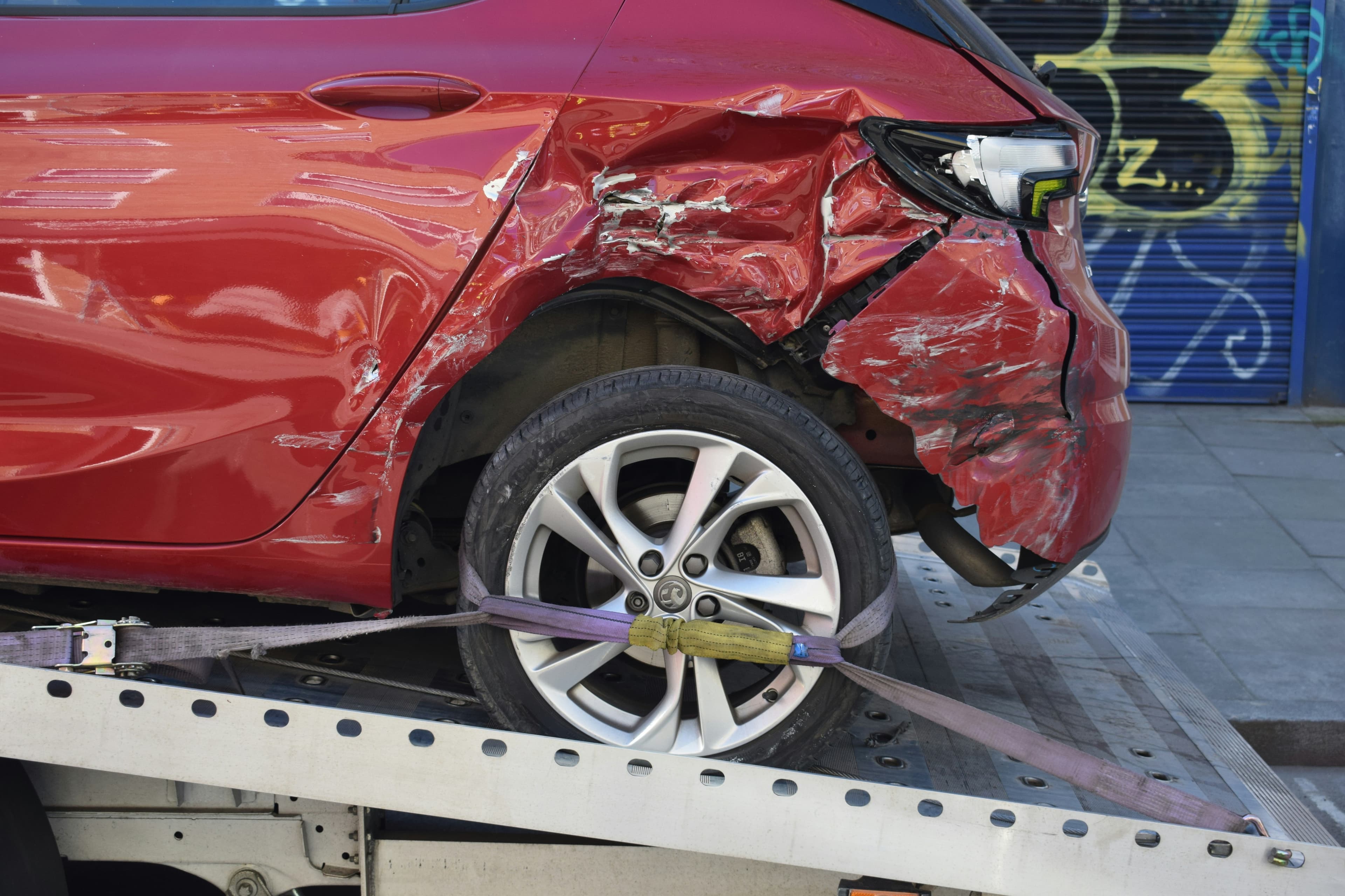 Accident-damaged red car strapped onto a flatbed recovery truck
