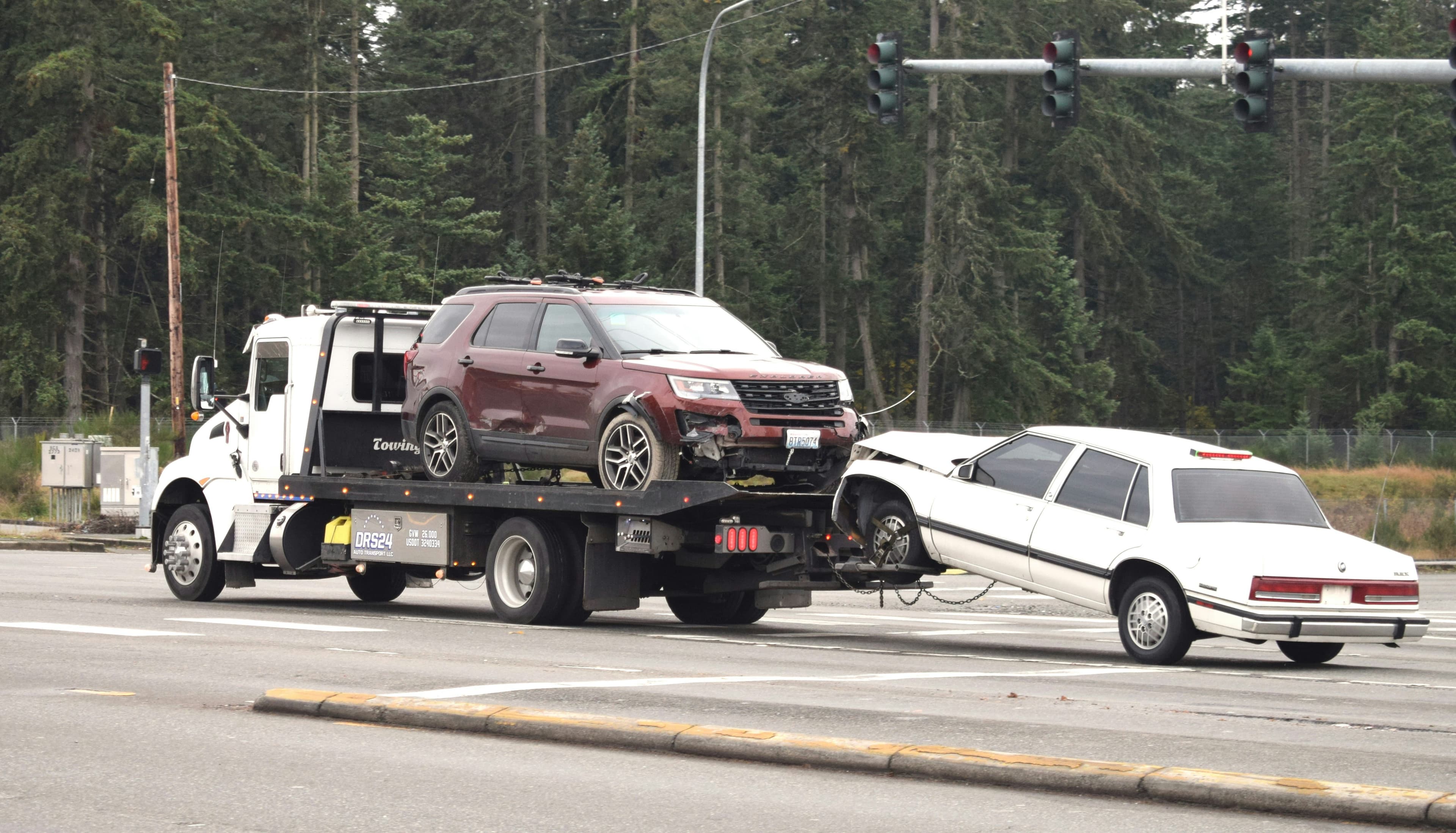 Flatbed recovery truck carrying an SUV and towing a damaged car